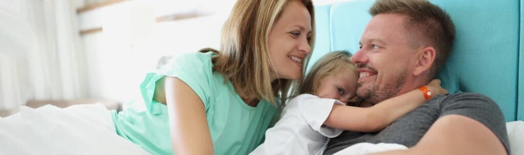 Padre, madre y bebé en la cama sonriendo